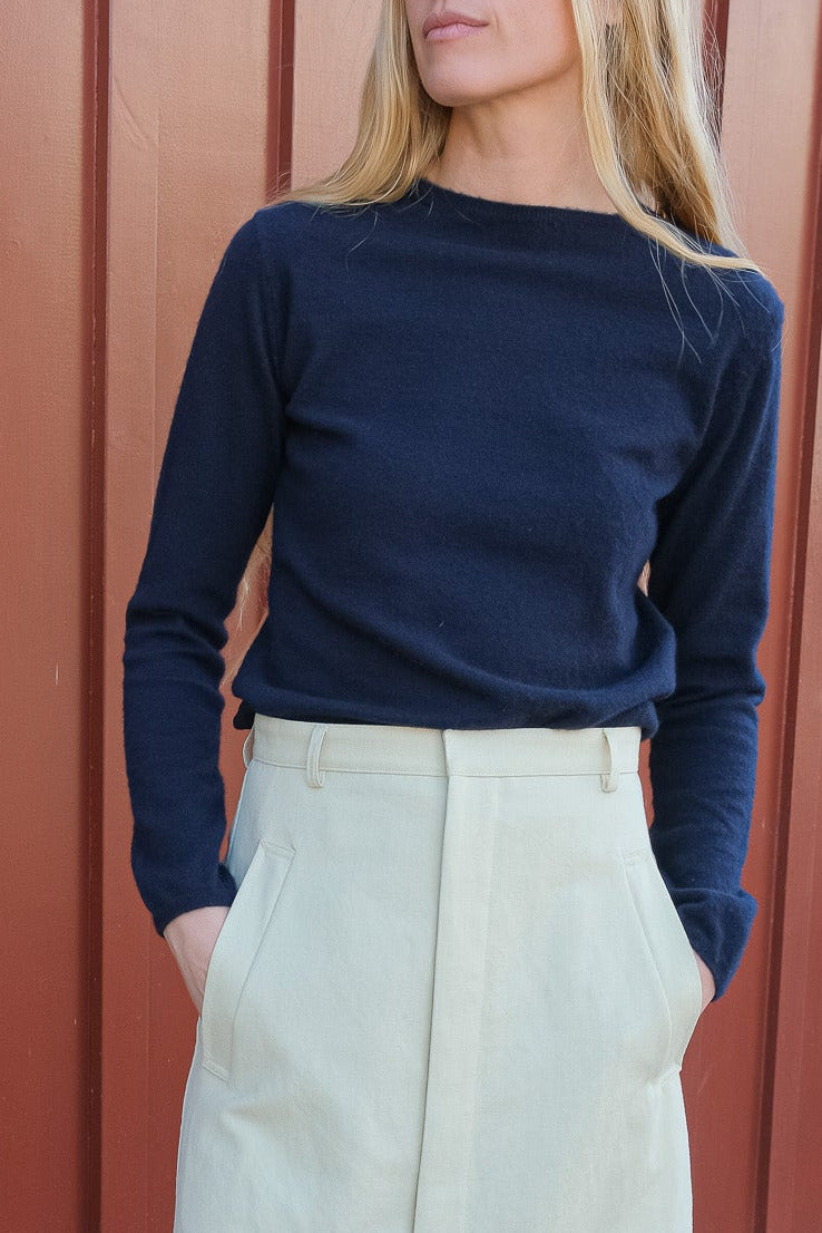 Person wearing a navy sweater and light-colored pants against a red-brown wall.