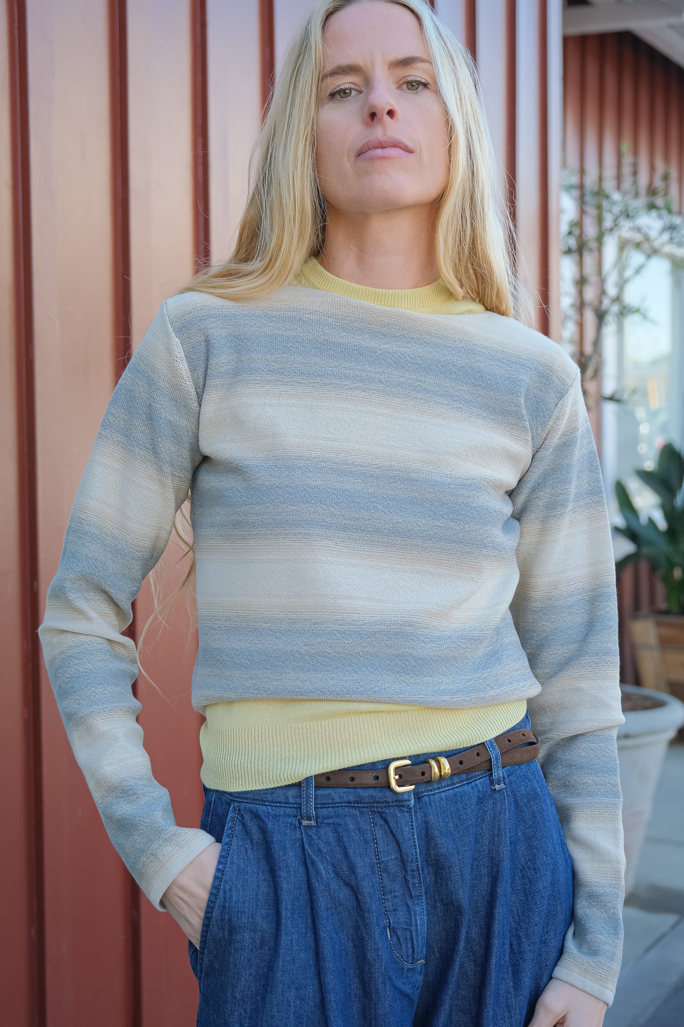 Woman wearing a striped sweater and blue pants standing in front of a wooden wall.