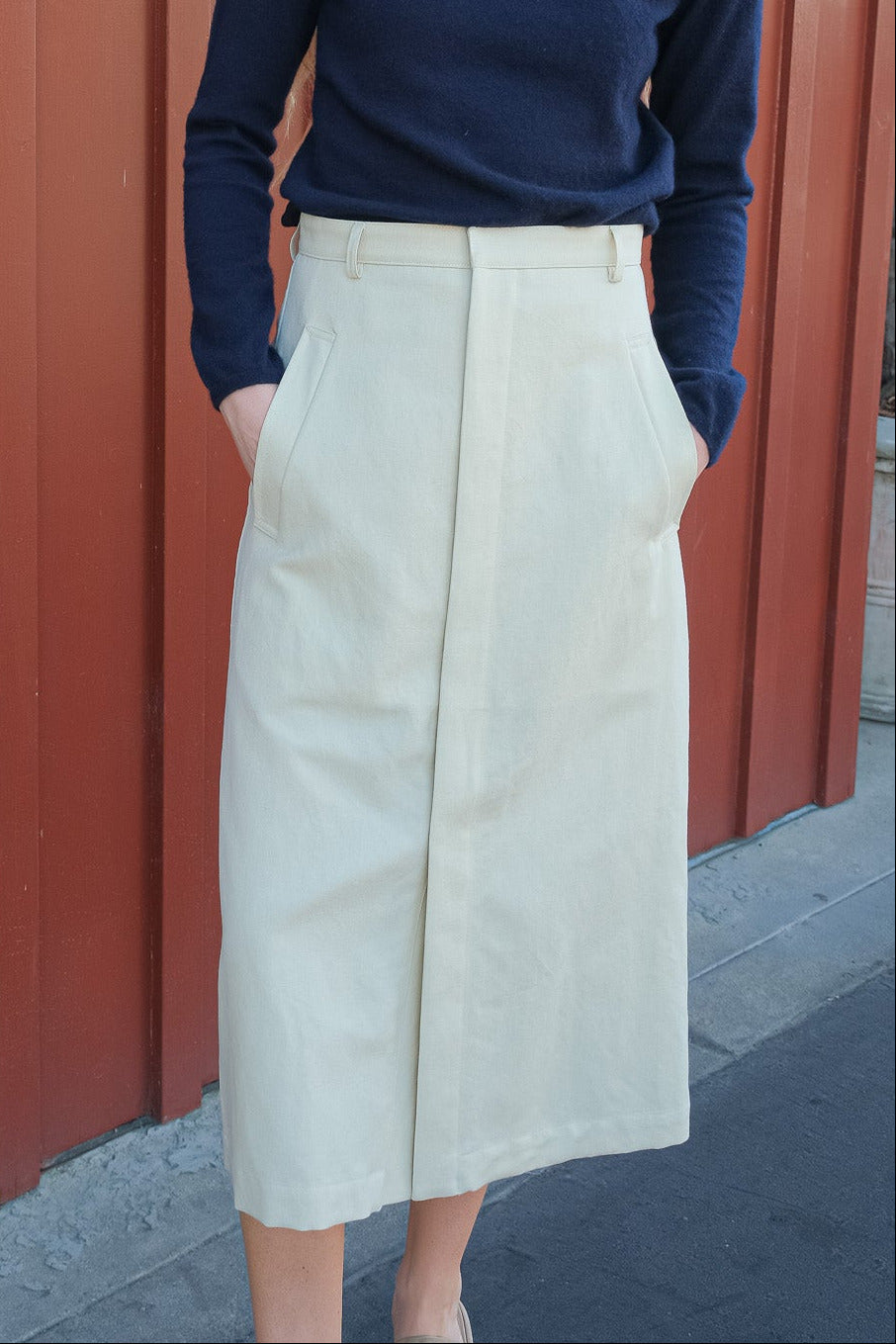 Person wearing a navy sweater and light-colored skirt against a red wall.