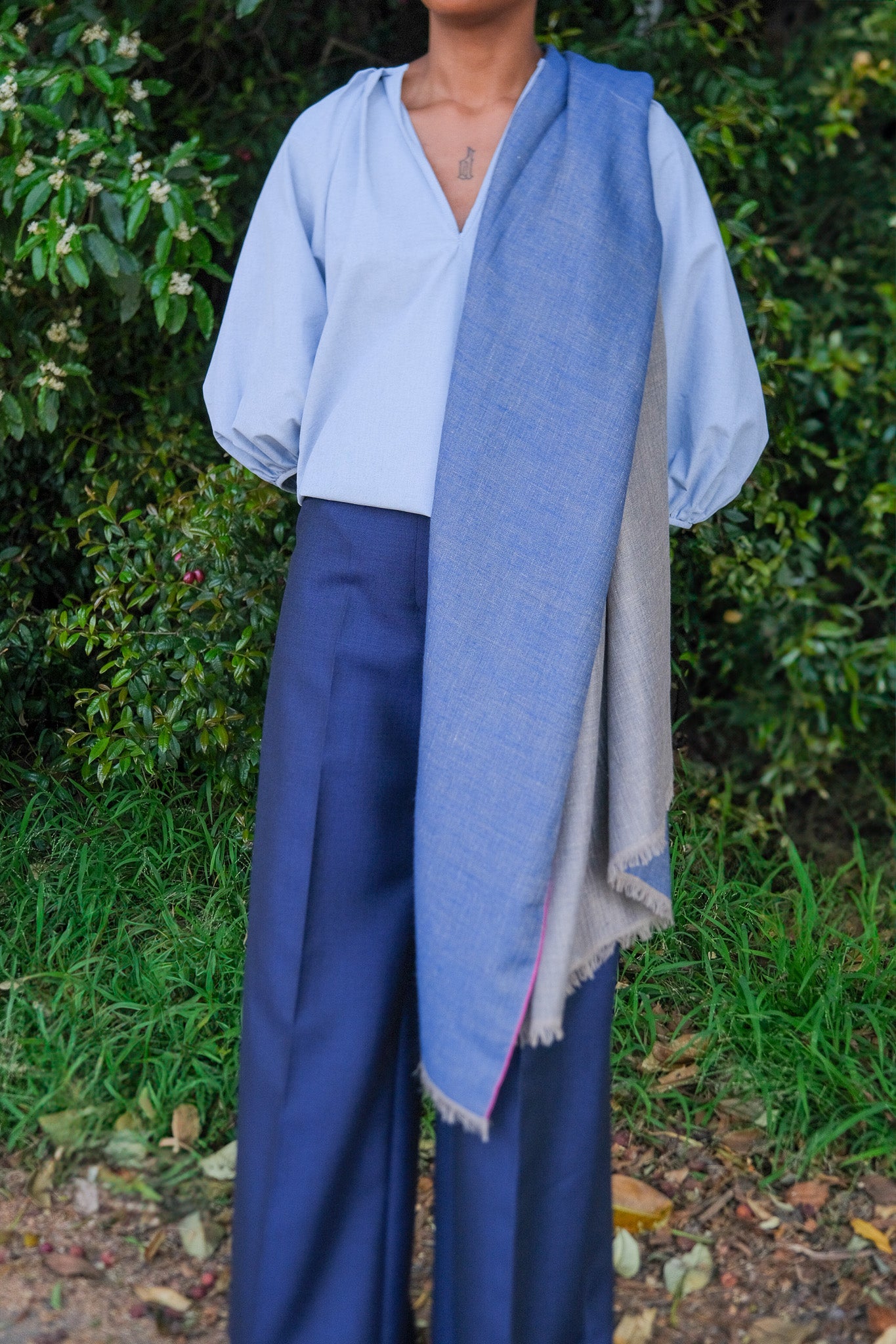 Person wearing a light blue shirt, dark blue pants, and a matching blue scarf outdoors.