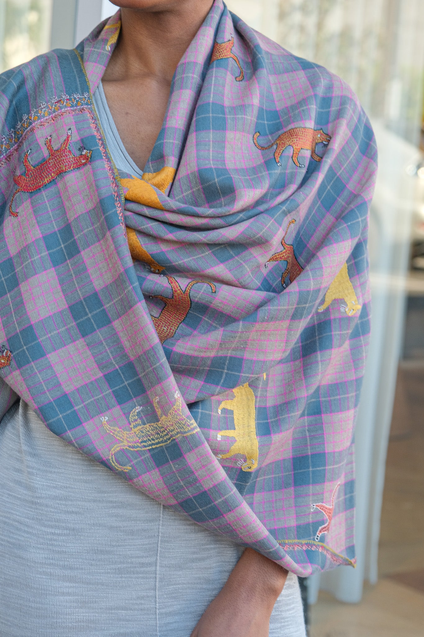 Yaser Shaw animal embroidered shaw on pink and grey plaid background. Available in Brentwood, CA and Charlotte, NC.