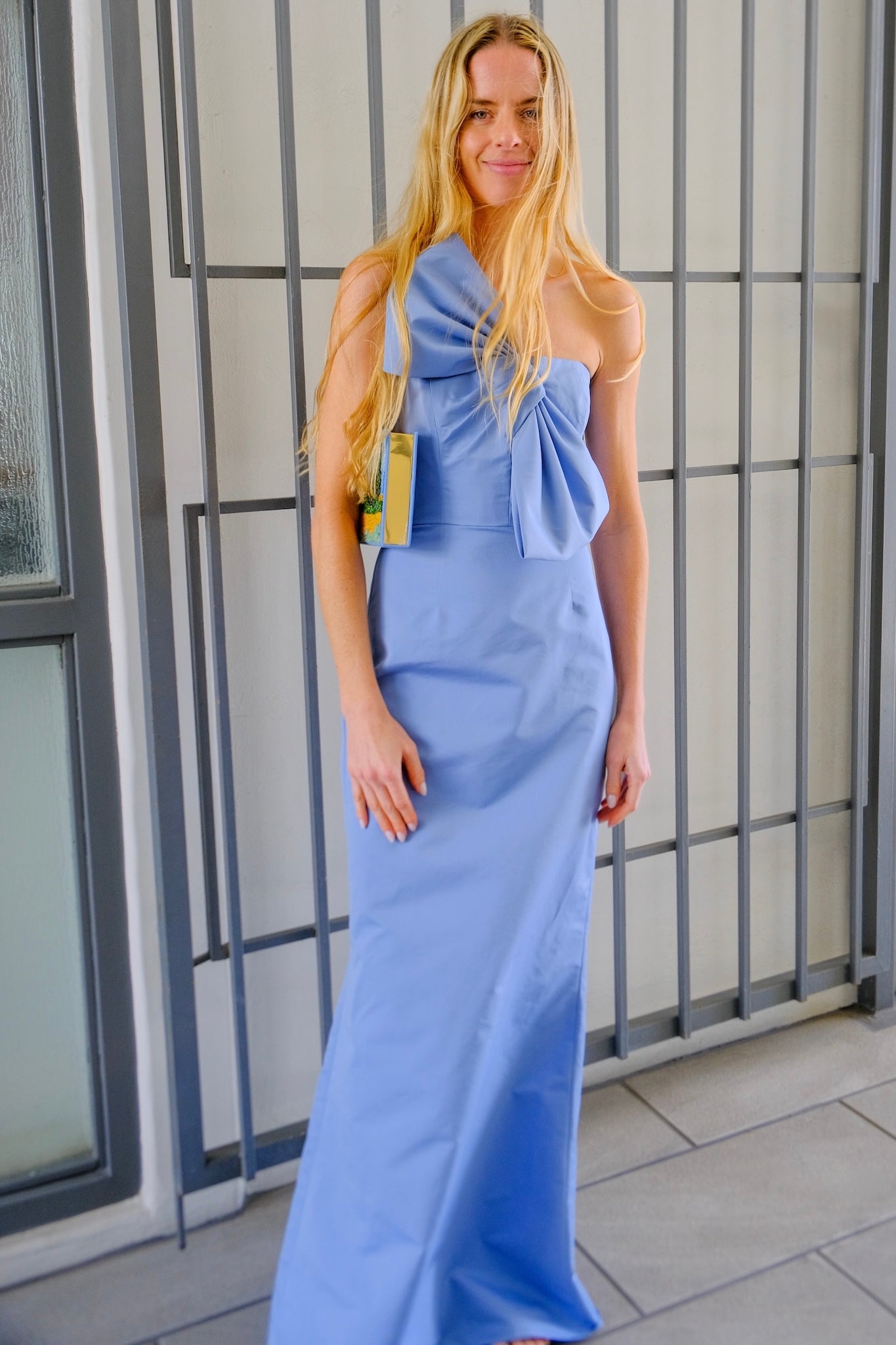 Blue cotton-silk bow-detail evening gown from Alejandra Alonso Rojas with a slim column silhouette and sculptural bow accent. Available in Brentwood, CA and Charlotte, NC.