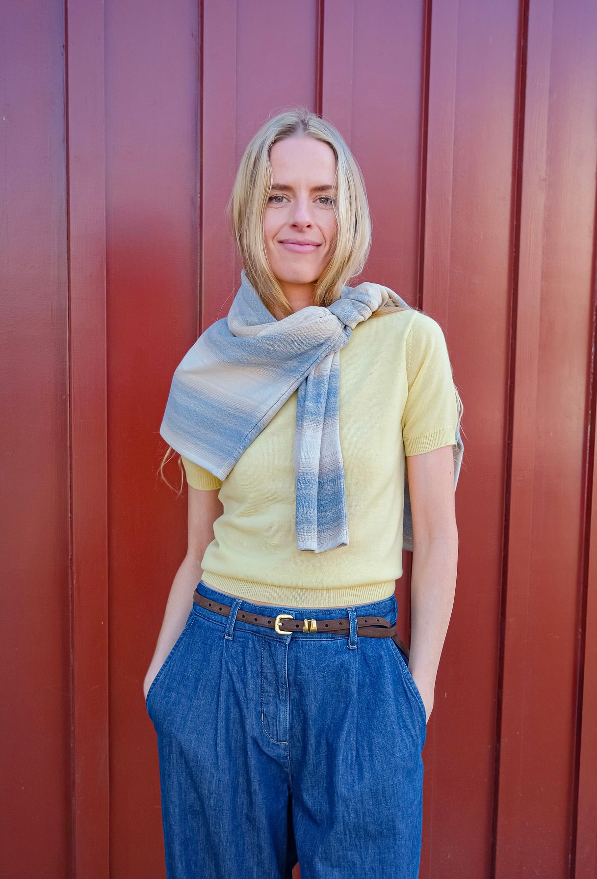 Woman wearing a yellow shirt, blue jeans, and a plaid scarf against a red background