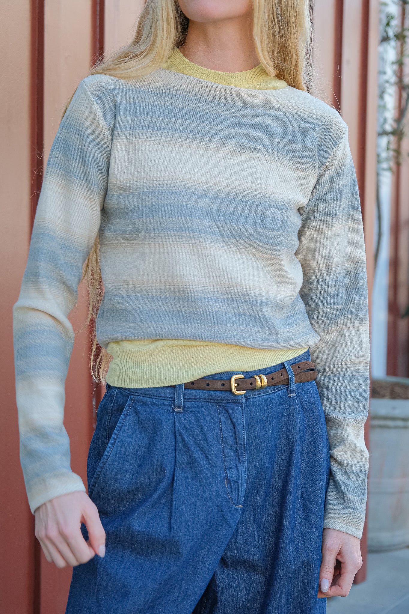 Person wearing a striped sweater and blue jeans with a blurred background