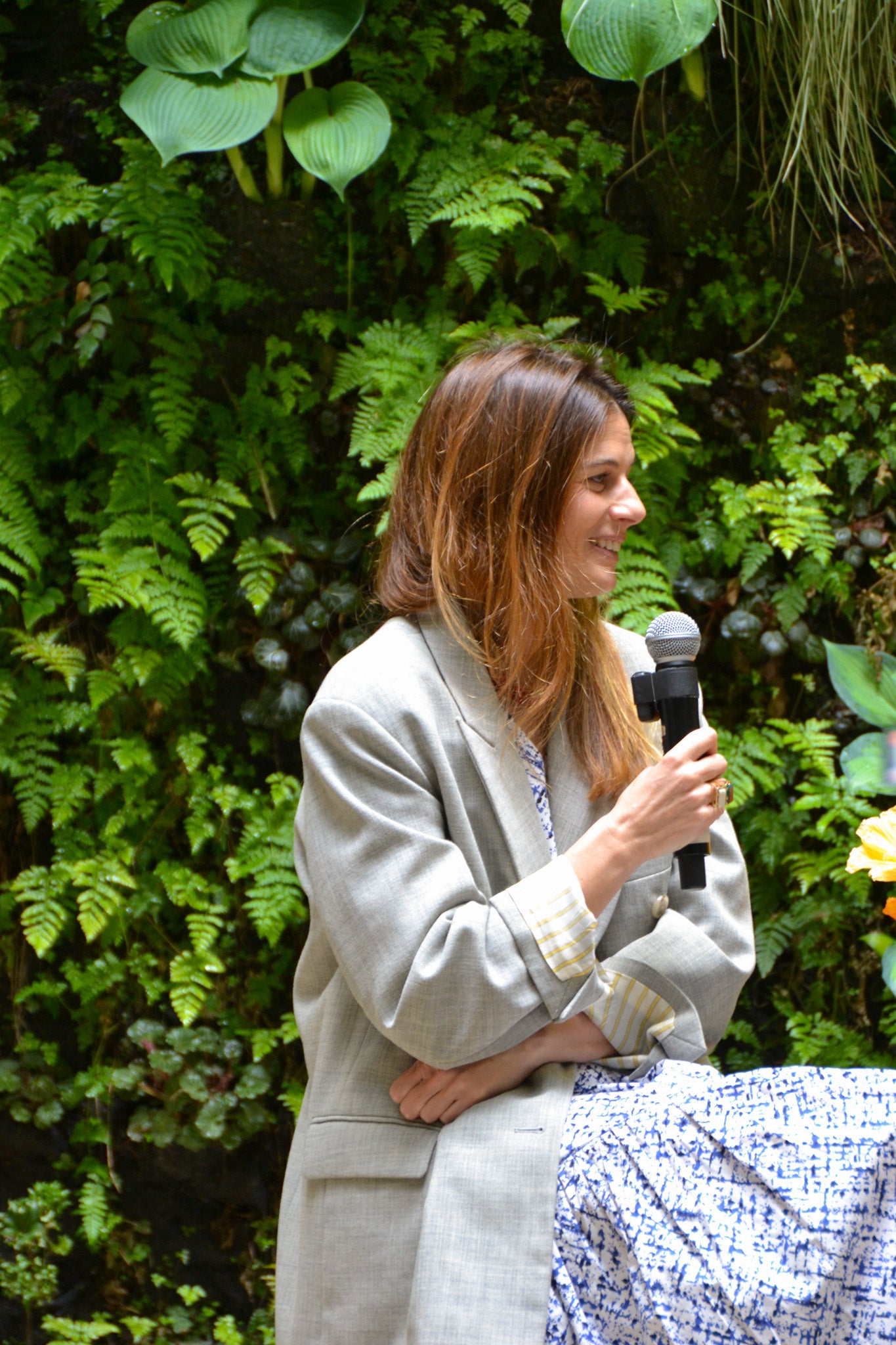 Woman holding a microphone in front of green foliage