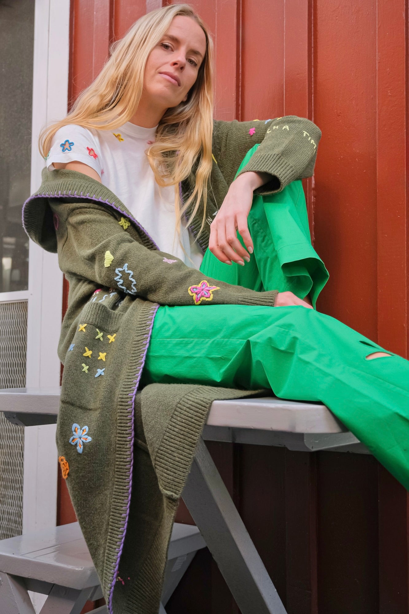 Woman wearing a green cardigan with floral patterns sitting on a bench.