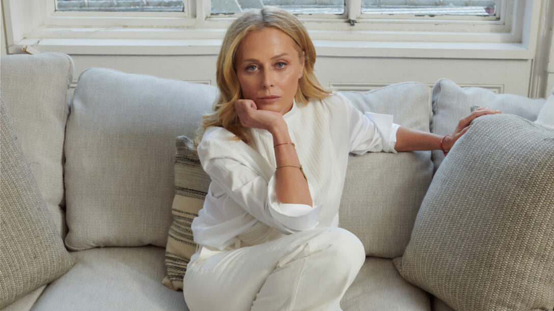 Woman in a white outfit sitting on a beige sofa in a bright room.